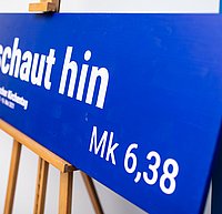 Das Motto "schaut hin" auf einem blauen Plakat